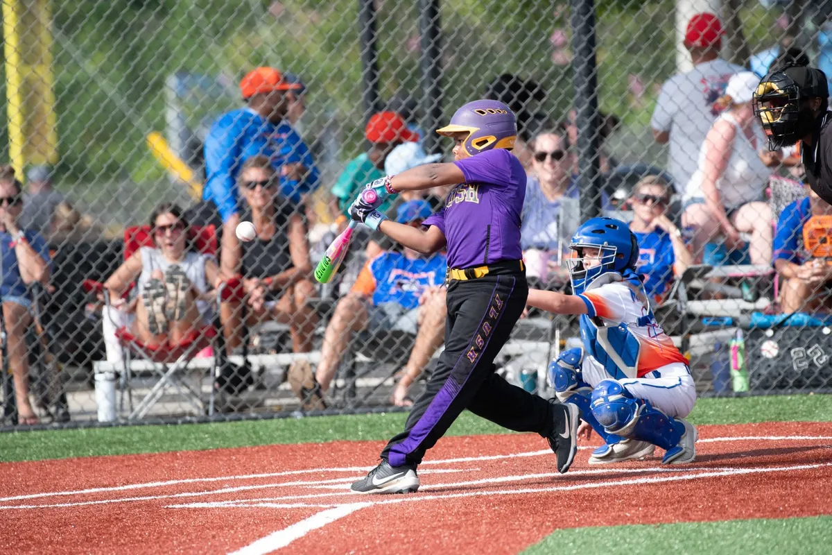 A young batter swings during a baseball game while a catcher waits.